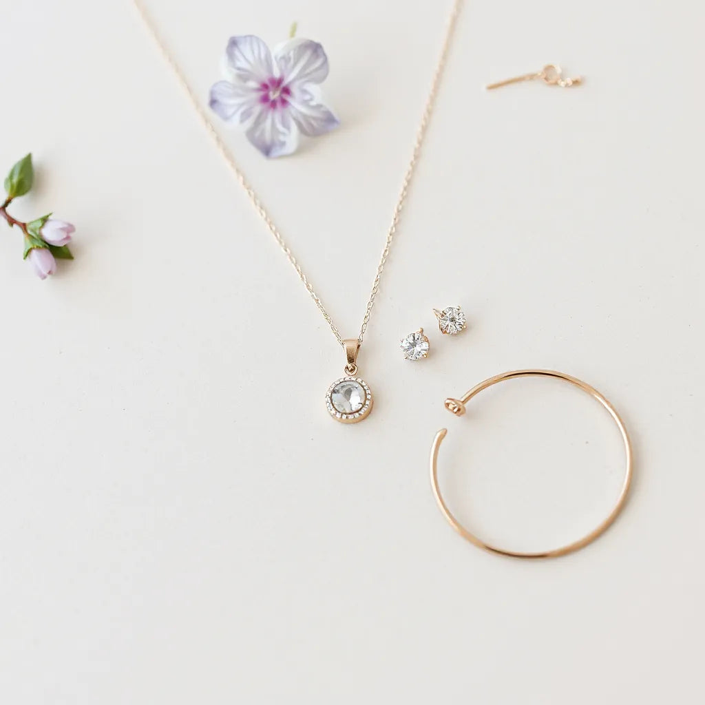 Delicate pendant necklace, stud earrings, and bracelet arranged on a neutral background with soft sparkle