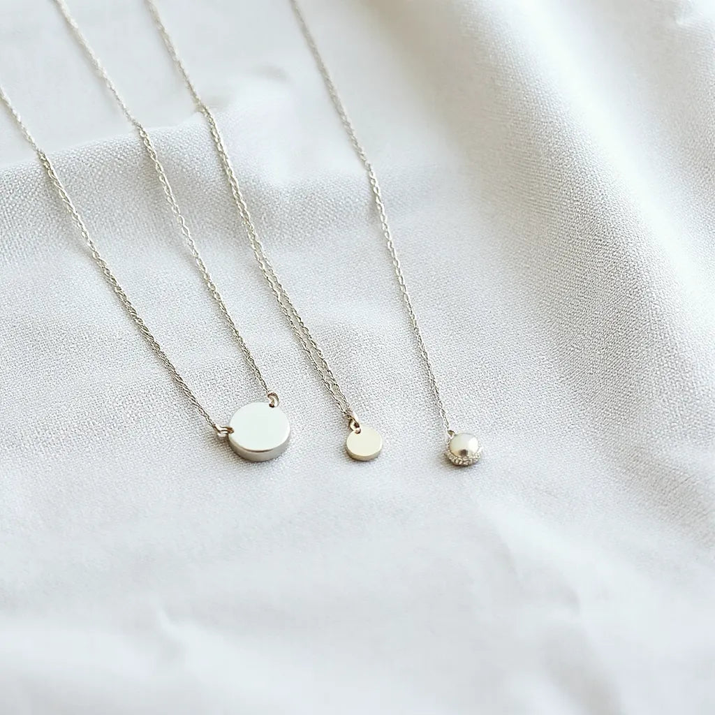 Three 925 sterling silver necklaces with different chain styles and a small pendant on light fabric