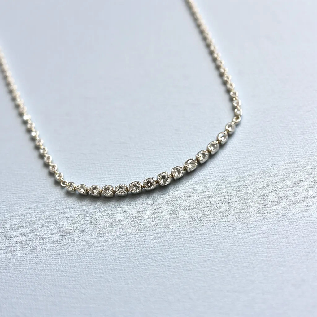 Moissanite tennis chain necklace with evenly set stones catching soft studio light on light fabric