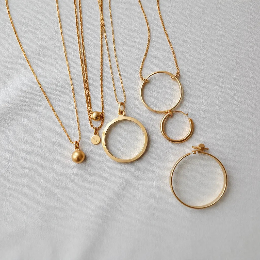 Gold plated necklace, hoop earrings, and bracelet arranged on a light neutral surface